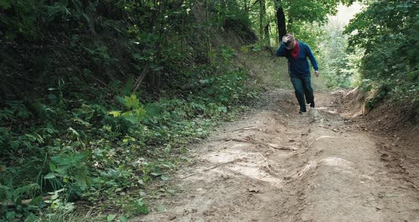 Hiker in a Cowboy Hat Walks a Steep Slope in the Middle of a Summer Forest