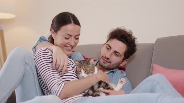 Happy couple relaxing on couchg, cuddling domestic cat