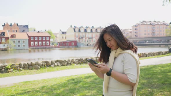 Asian woman with black straight hair and happy face. Standing and using smartphone