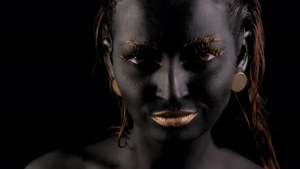 Closeup of a Young Beautiful Woman's Face with Black and Gold Paint on Her Skin