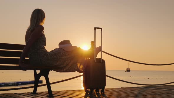 A Young Girl Is Waiting To Board a Ship in the Early Morning on a Sea Pier with Luggage