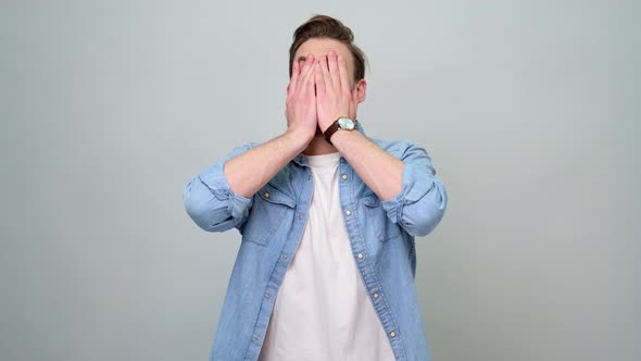 Confused young man in denim jacket over light grey background put palm on face facepalm gesture