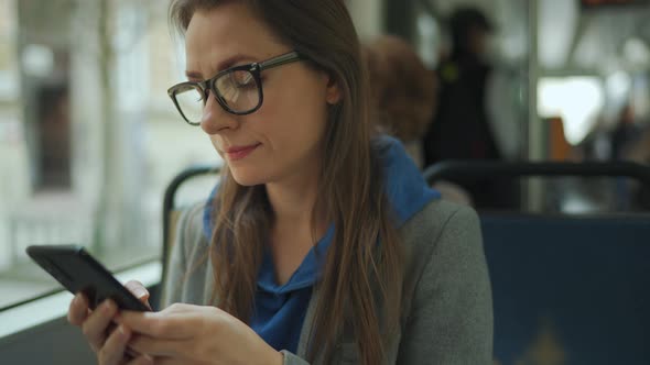 Woman with Glasses in Tram Using Smartphone Chatting and Texting with Friends