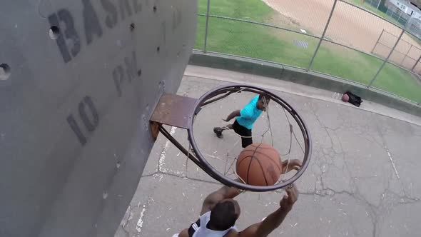 A young man basketball player dunking while playing one on one on an old outdoor basketball hoop