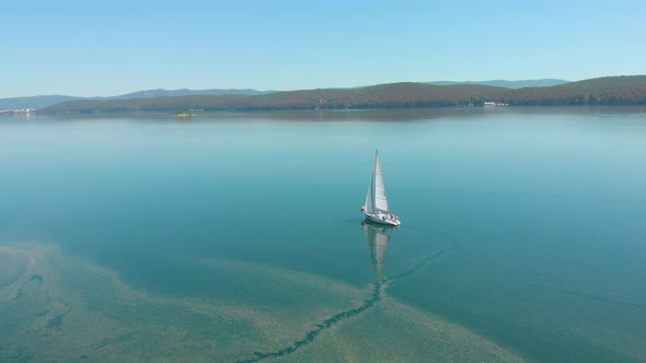 Aerial View of Sailing Boat Walking Alone on a Wide Blue Clear Lake on a Sunny Morning