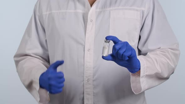 Doctor in a White Medical Suit and Protective Gloves Holds Vial with Coronavirus Vaccine in His Hand