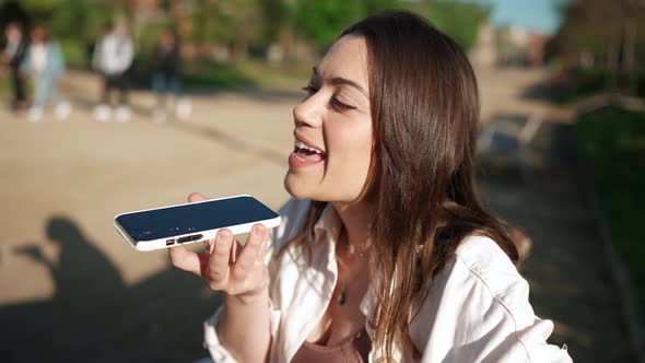 Positive brunette woman recording voice message on mobile