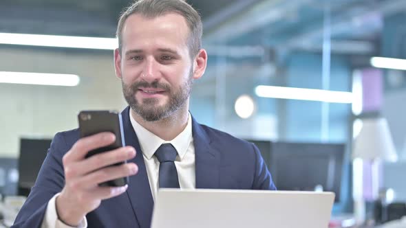 Portrait of Cheerful Businessman Using Smartphone in Office