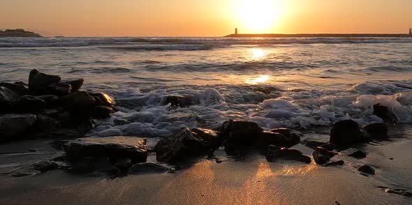 Slow motion shoot on sea waves on the rocks with lighthouse view at sunset