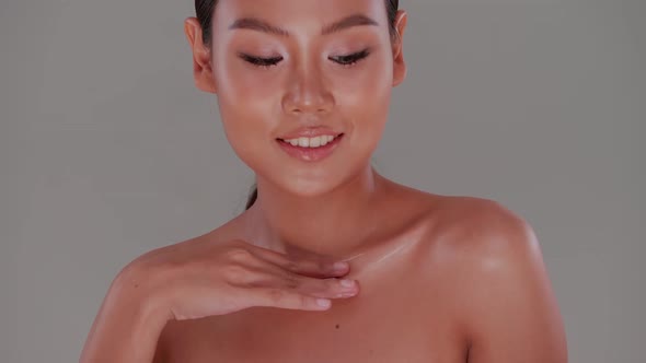 Beautiful girl applying moisturizer oil onto her body.  Asian young woman with tanned skin.