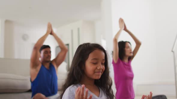 Hispanic parents and daughter sitting on the floor meditating at home