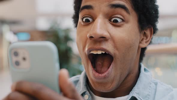 African Happy Excited Guy Surprised By Message Good News Winning Online Bets Looking at Mobile Phone
