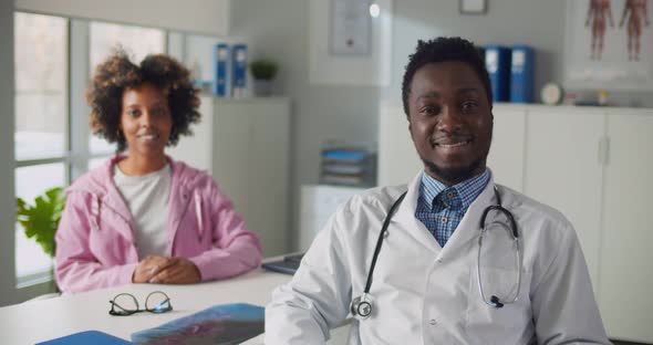 Portrait of Afroamerican Male Doctor and Female Patient Smiling at Camera in Clinic Office