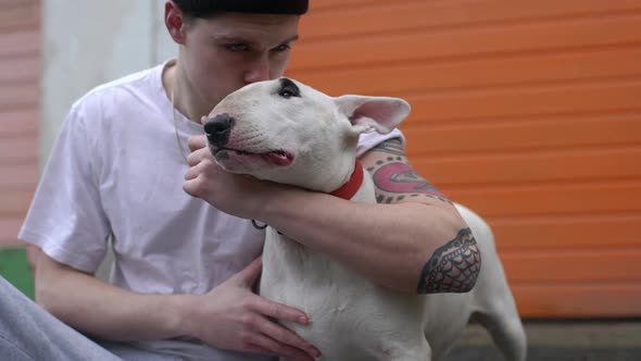 Portrait of Young Man in Casual Sitting on Pavement in Companion of His Bull Terrier Hugging and