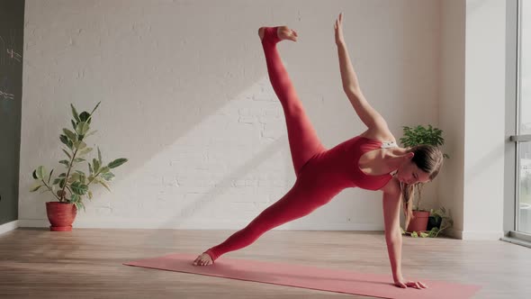 Young Woman in Red Sports Uniform Does Vasisthasana in Yoga Studio
