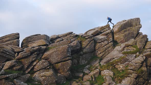 Backpacker climbing down rock formations in Dartmoor national park moorland, England, in the evening