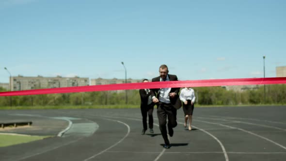 An Adult Businessman in a Suit Runs Through an Open Stadium Competing with Office Workers