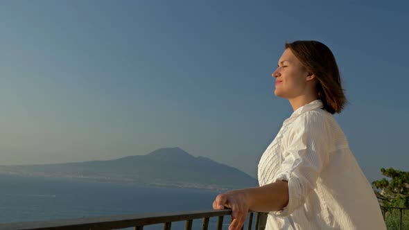 Young Woman Stands on a Balcony with a Beautiful View of the Sea and Mountains