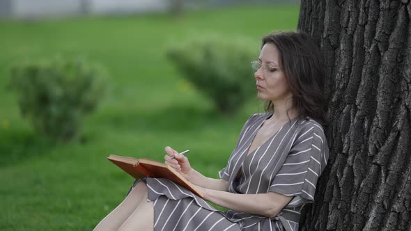 Beautiful Adult Student Doing Her College Homework Sitting on the Grass in the City Park