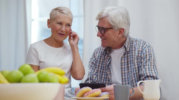 Aged Couple Listening To Music at Digital Tablet While Having Delicious Breakfast at Home Kitchen