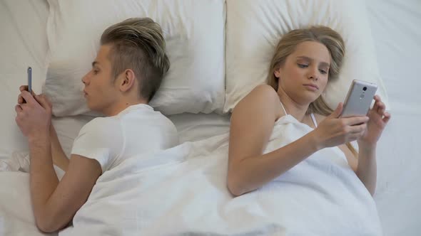 Young Couple Surfing Internet on Mobile in Bed Lying Back to Back, Indifference