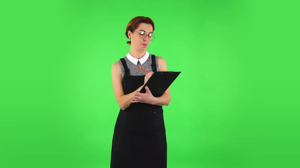 Funny Girl in Round Glasses Is Writing Plans at Black Folder with Pencil. Green Screen