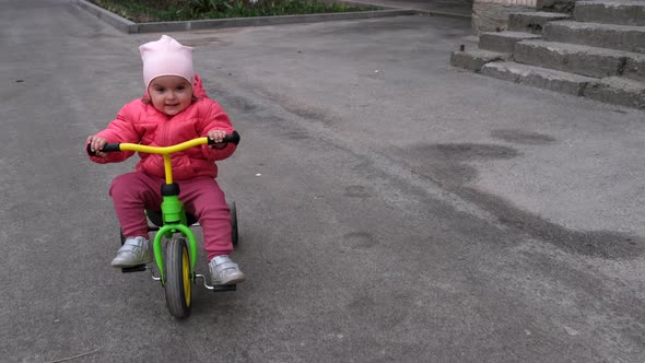 Toddler girl who rides a tricycle down the street. Slow motion.
