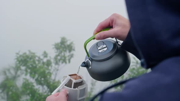 Closeup hands of young tourist man pouring hot water into a cup with coffee on the mountain peak.