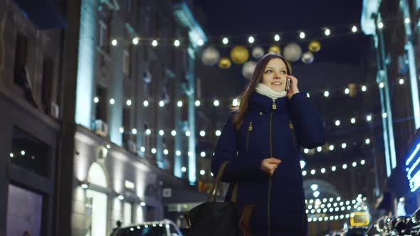 A Beautiful Young Woman Walks Through the Night City Talking on the Phone