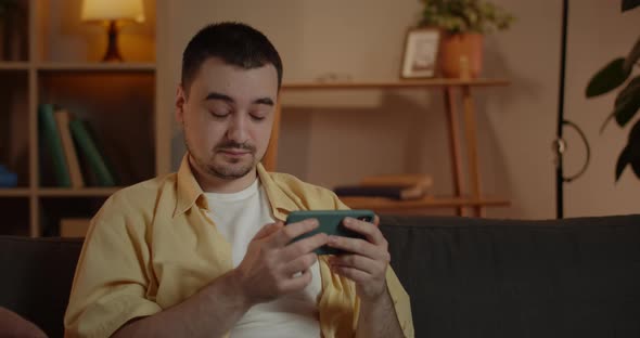 Crop View of Concentrated Man Watching Video While Sitting on Sofa in Evening at Home