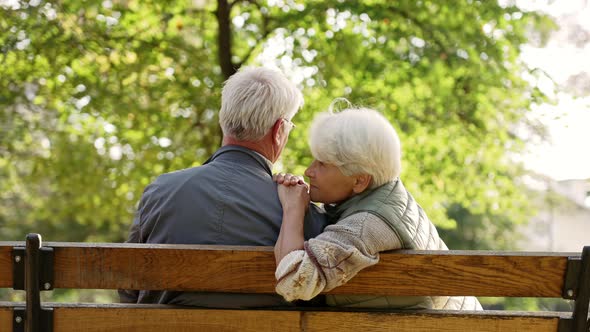 Two Elderly Greyhaired Caucasian People Sitting on a Bench in Park and Deepening Their Relationship