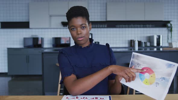 African american businesswoman having video chat going through paperwork in workplace kitchen