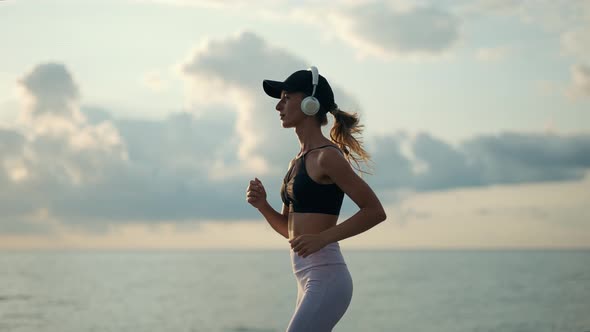 A Young Woman Runner is Listening to Music in Earphones and Training By a Sea