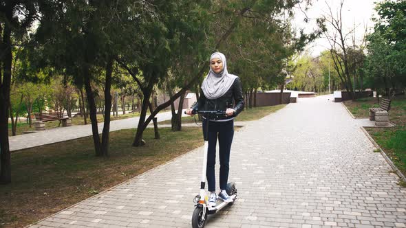 Modern Muslim Woman with a Hijab Riding Escooter in the Park