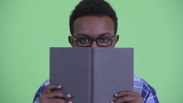 Shy Young African Hipster Man Thinking While Hiding Behind Book