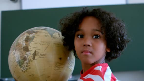 Front view of African American schoolboy with globe in a classroom at school 4k
