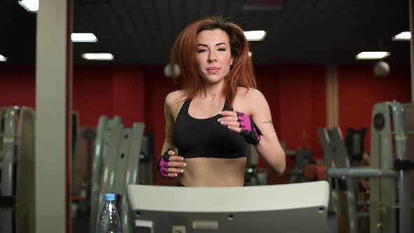 Slowmotion of a young woman jogging on a treadmill in a gym, close-up