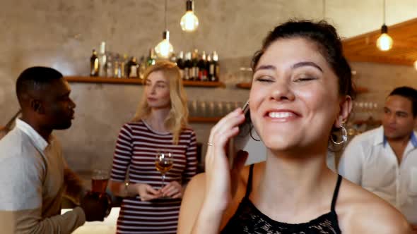 Young smiling woman talking on phone while friends interacting in background 4K 4k