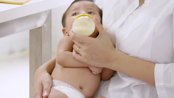 Young mother feeding newborn baby from milk bottle