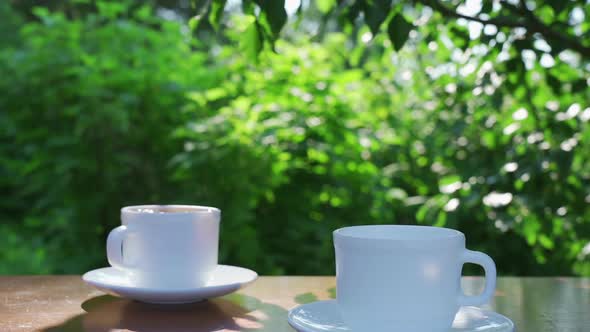 Pouring Coffee Into Two Cups on a Table in a Garden Landscape