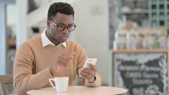 African American Man Using Smartphone While Drinking Coffee in Cafe