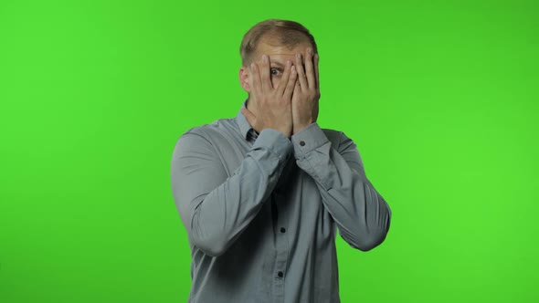 Shy Guy Scared To Watch. Man Covering Eyes with Hands and Looking Cautiously Curious at Camera