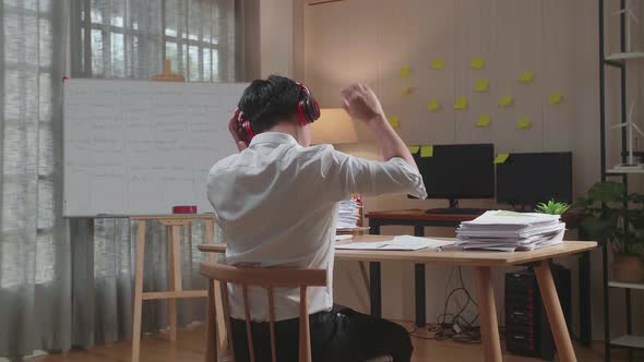 Back View Of Man Wearing Headphones To Listen To Music Before Dancing After Working With Documents