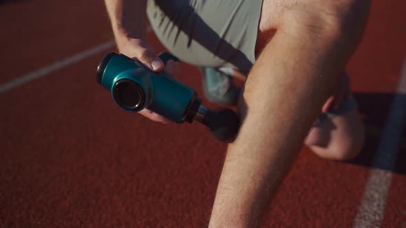 An Athlete Massages with a Percussion Therapy Gun to Relieve the Pain of Muscle Aches After a