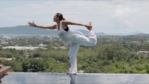 Barefooted Woman in Standing Bow Pose Near Swimming Pool Against Green Forested Islands