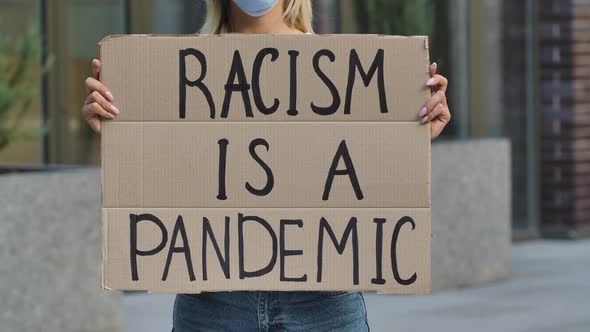 RACISM IS A PANDEMIC on a Cardboard Poster in the Hands of Female Protester Activist. Closeup of