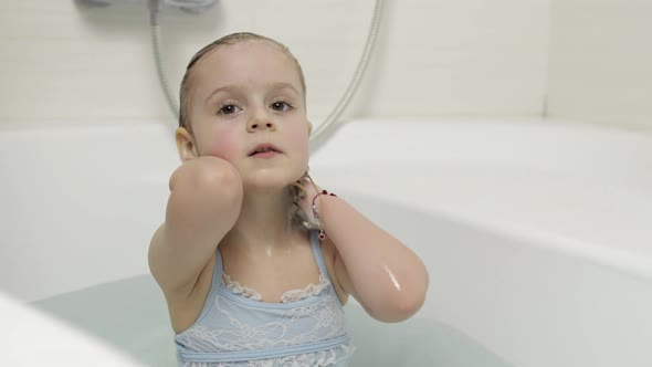 Cute Blonde Girl Takes a Bath in Swimwear. Little Child Washes Her Head