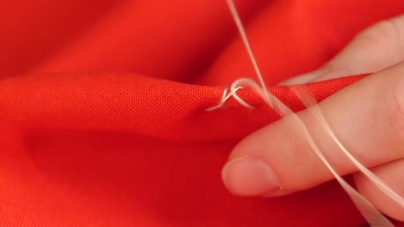 Woman`s Hands Sewing with Needle, White Thread and Thimble on Red Cloth, Close Up, Slow Motion