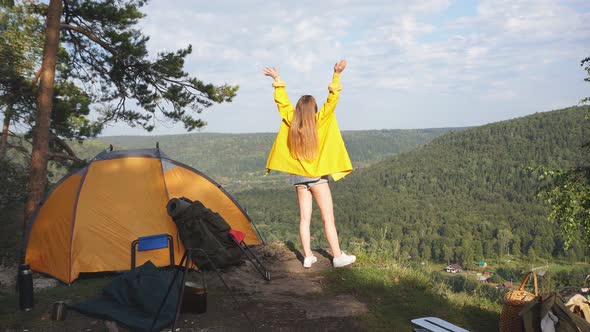 Young Tourist in Yellow Raincoat Stands on Top of the Mountain