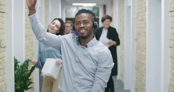 Portrait of Positive Smiling African American Man Dancing in Office Corridor with Caucasian